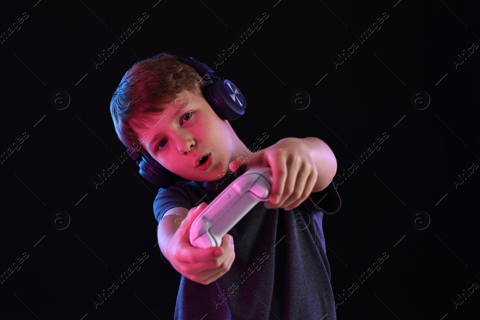 Photo of Cute little boy in headphones playing video game with controller on black background