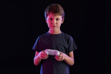 Little boy playing video game with controller on black background