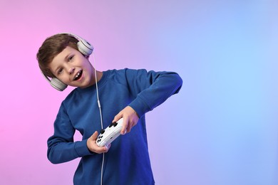 Happy little boy in headphones playing video game with controller on color background. Space for text