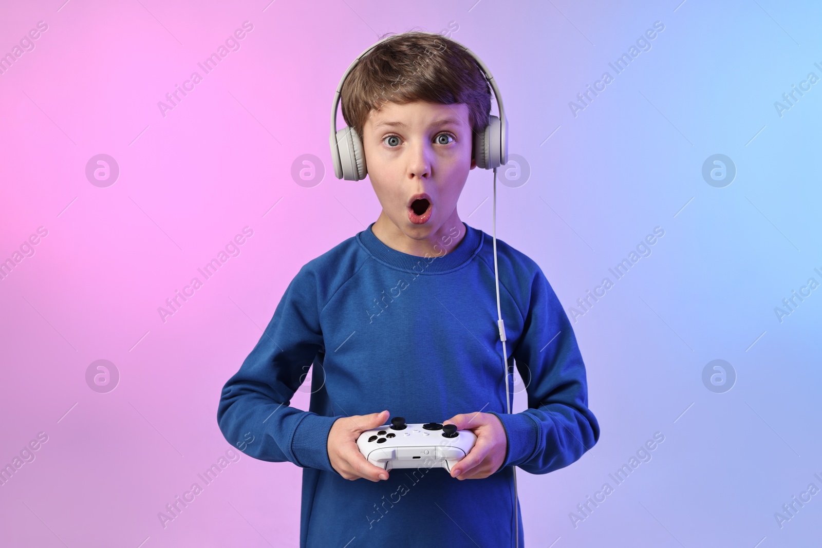 Photo of Cute little boy in headphones playing video game with controller on color background