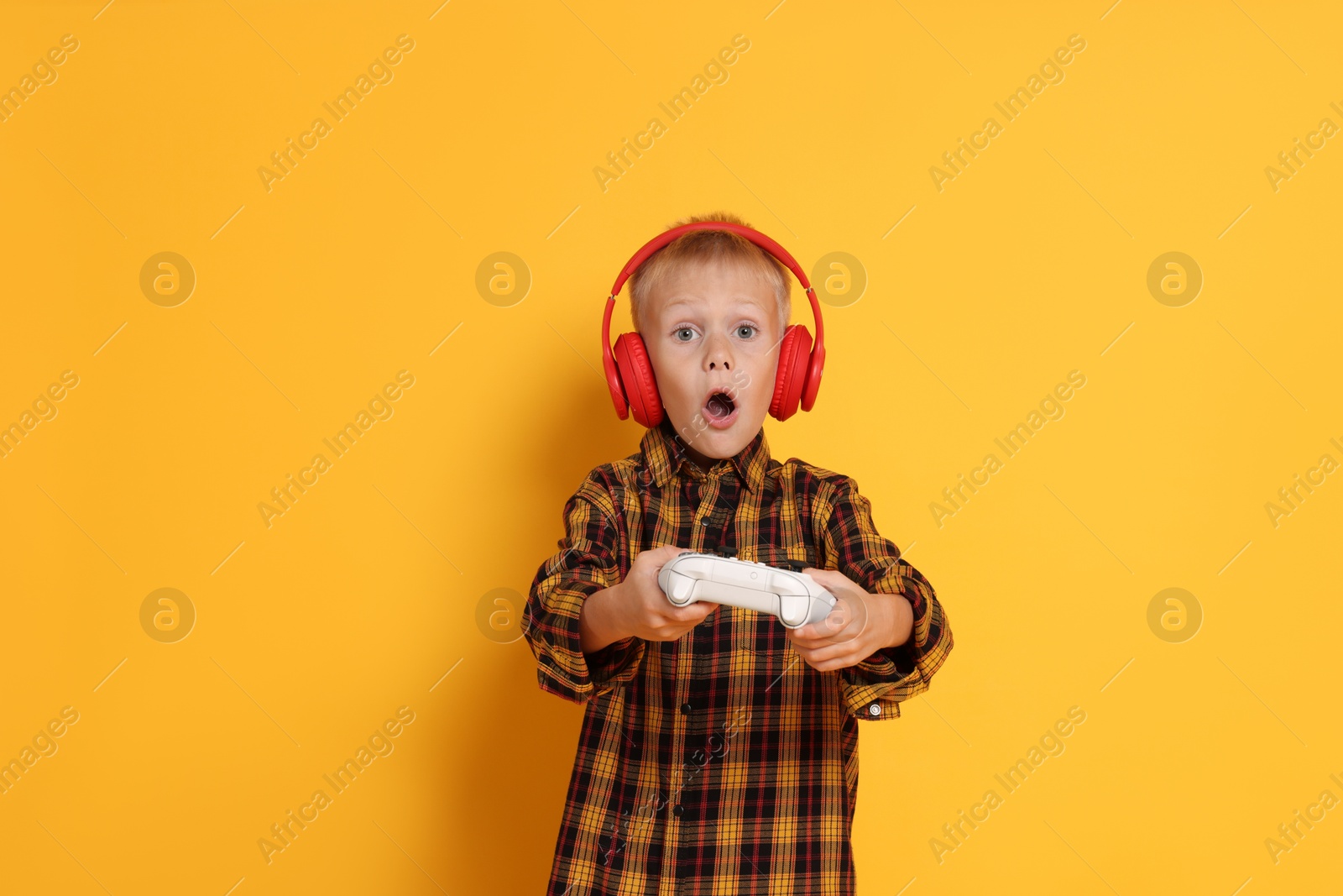 Photo of Cute little boy in headphones playing video game with controller on orange background. Space for text