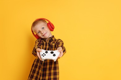 Photo of Cute little boy in headphones showing controller on orange background. Space for text