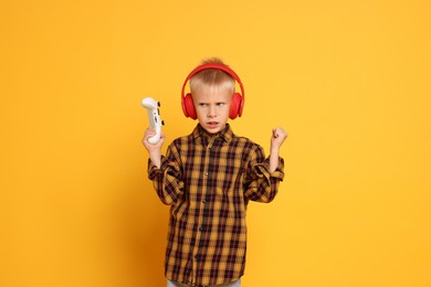 Photo of Little boy in headphones with controller on orange background