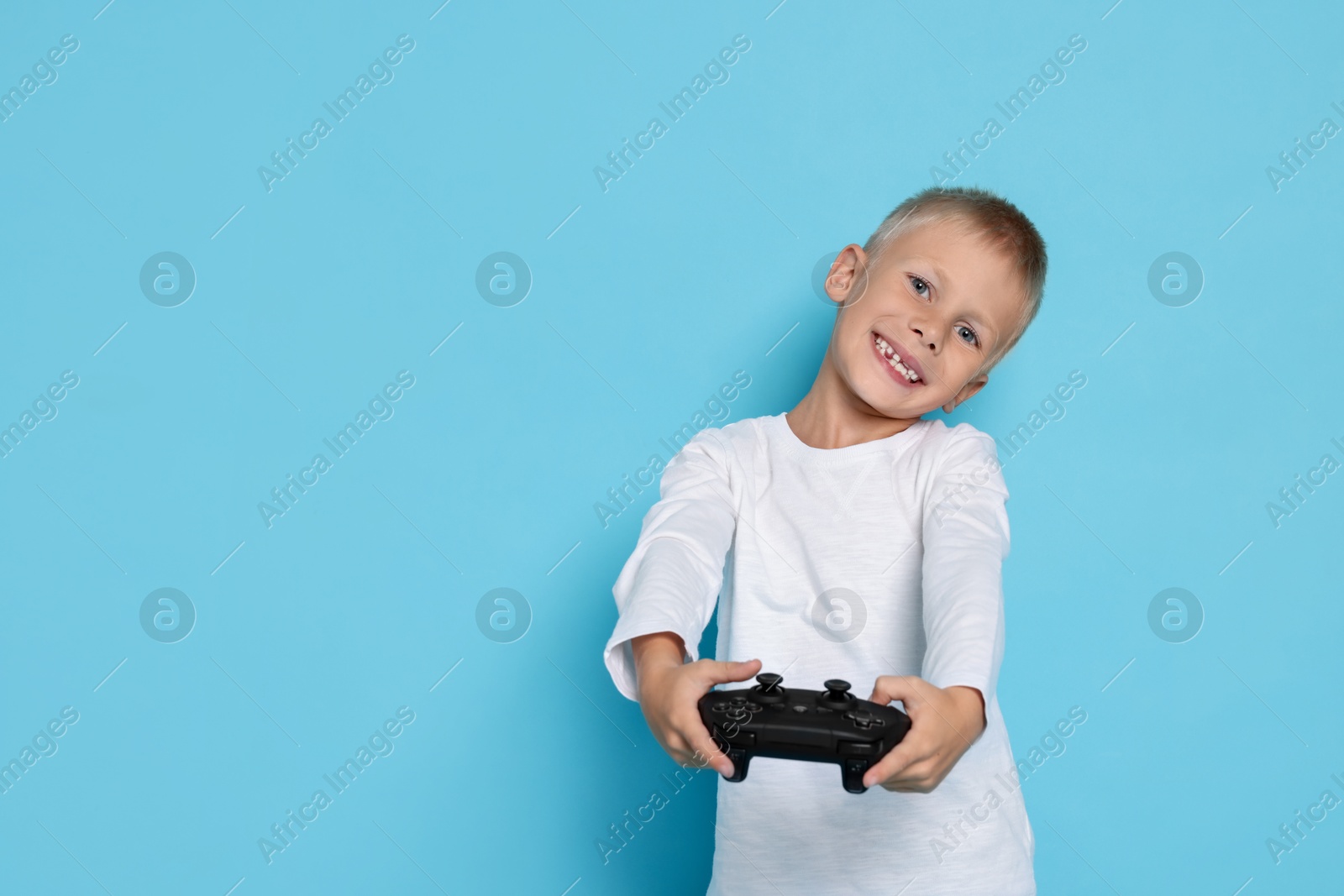 Photo of Happy little boy playing video game with controller on light blue background. Space for text