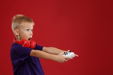 Cute little boy playing video game with controller on red background. Space for text