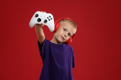 Cute little boy in headphones showing controller on red background