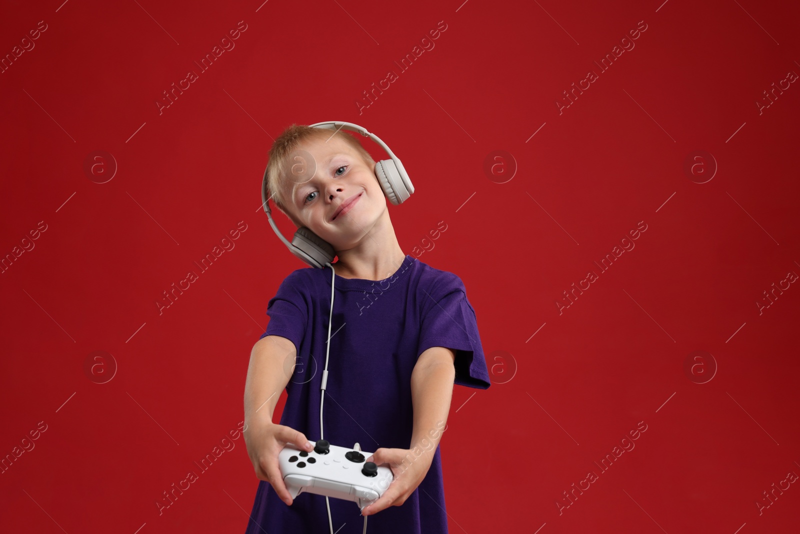 Photo of Cute little boy in headphones playing video game with controller on red background. Space for text