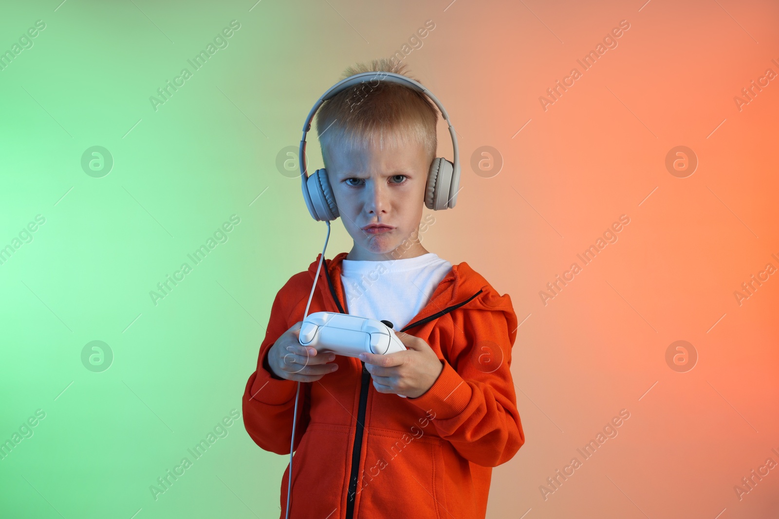 Photo of Cute little boy in headphones playing video game with controller on color background