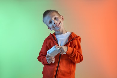 Happy little boy playing video game with controller on color background