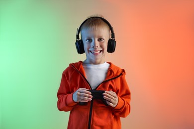 Photo of Happy little boy in headphones with controller on color background