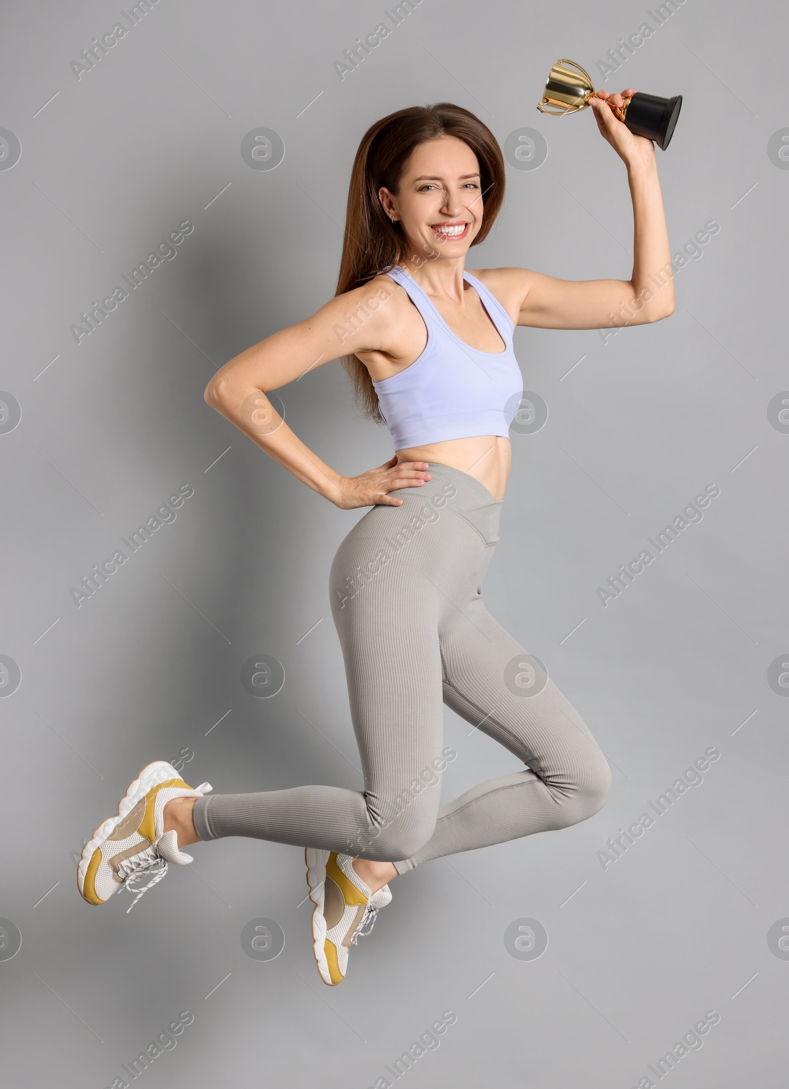 Photo of Happy winner with gold trophy cup jumping on gray background