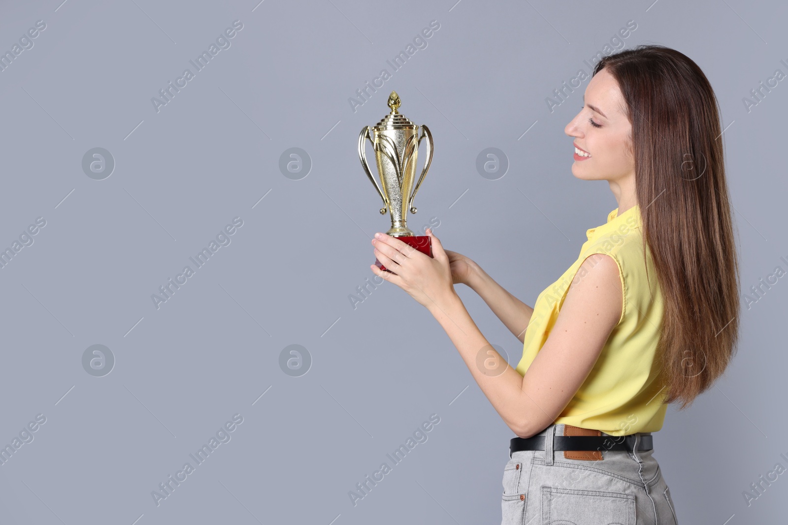 Photo of Happy winner with gold trophy cup on gray background, space for text