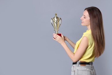 Photo of Happy winner with gold trophy cup on gray background, space for text