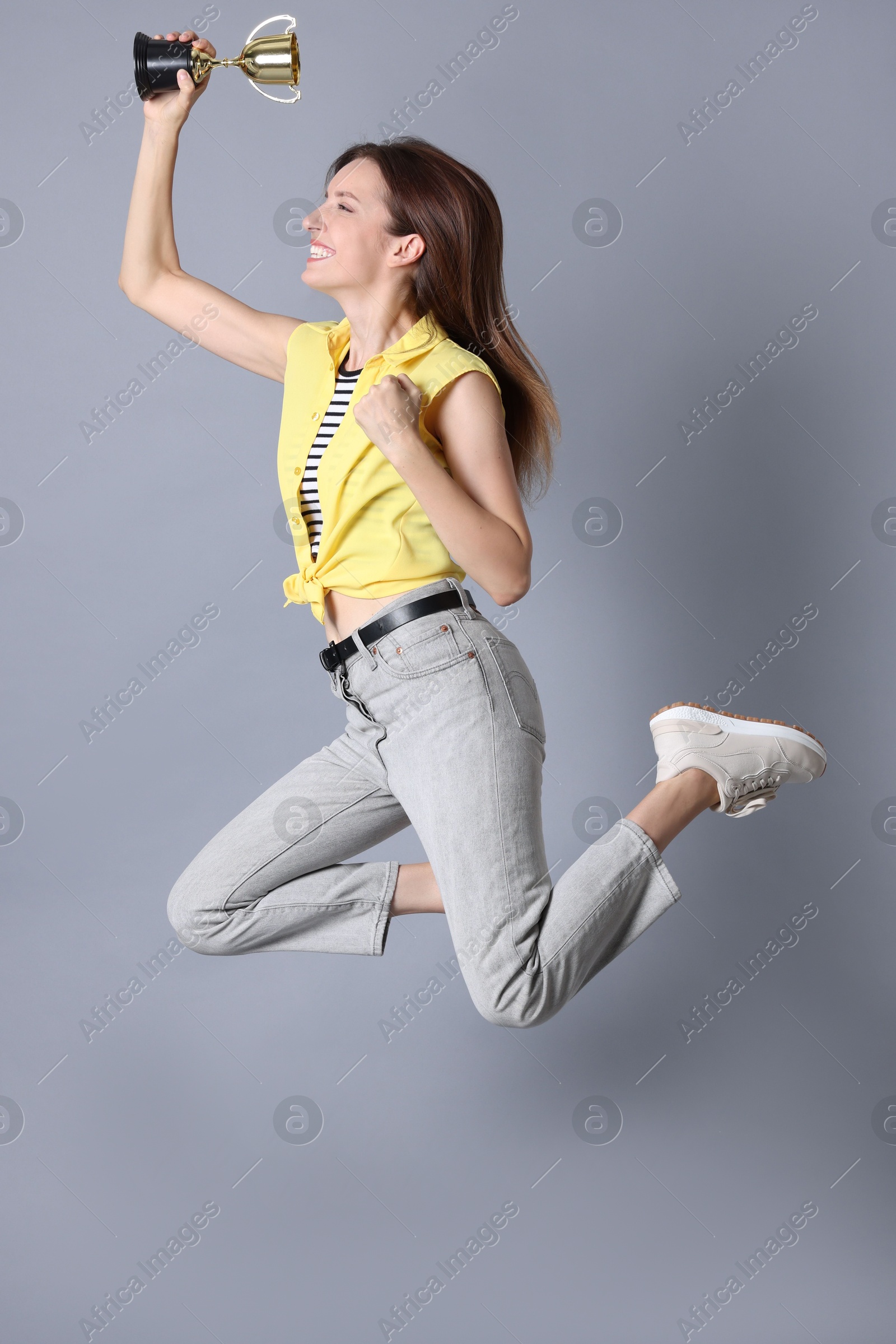 Photo of Happy winner with gold trophy cup jumping on gray background