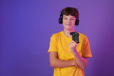 Teenage boy in headphones with controller on purple background. Space for text