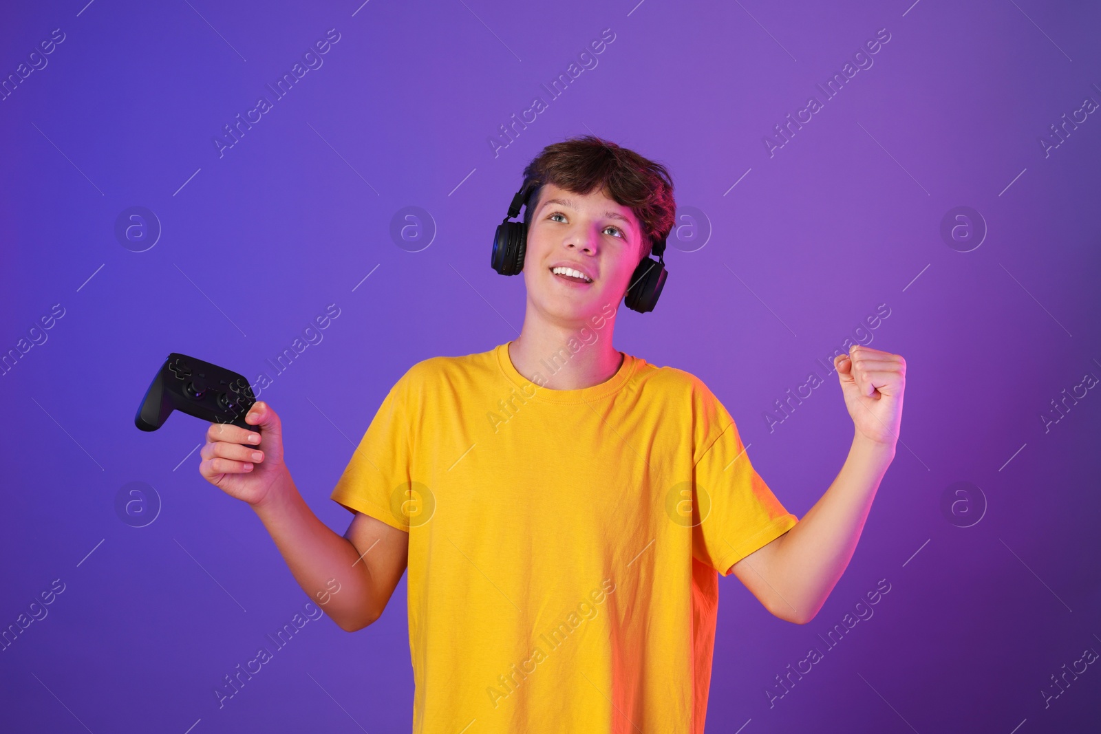 Photo of Happy teenage boy in headphones with controller on purple background