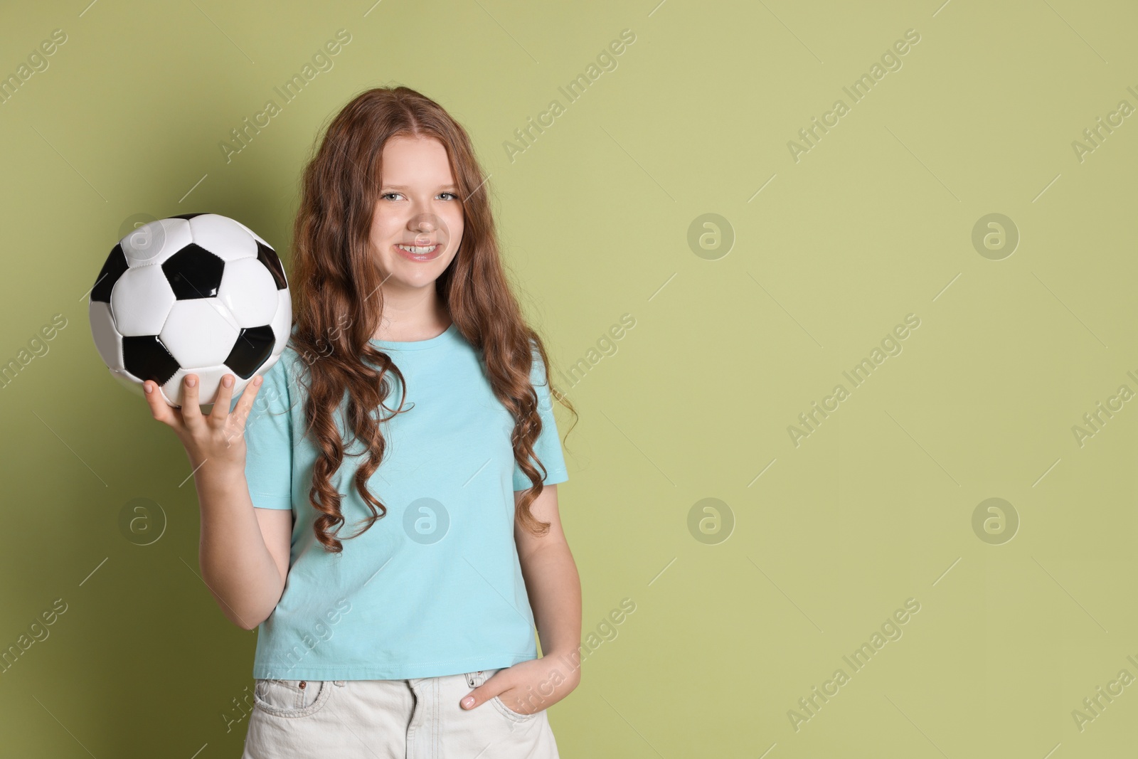 Photo of Smiling teenage girl with soccer ball on green background. Space for text