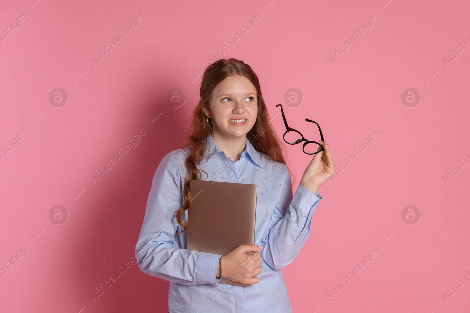 Photo of Smiling teenage girl with laptop and glasses on pink background