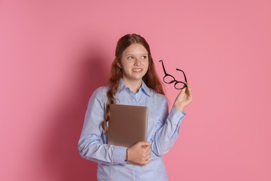 Photo of Smiling teenage girl with laptop and glasses on pink background