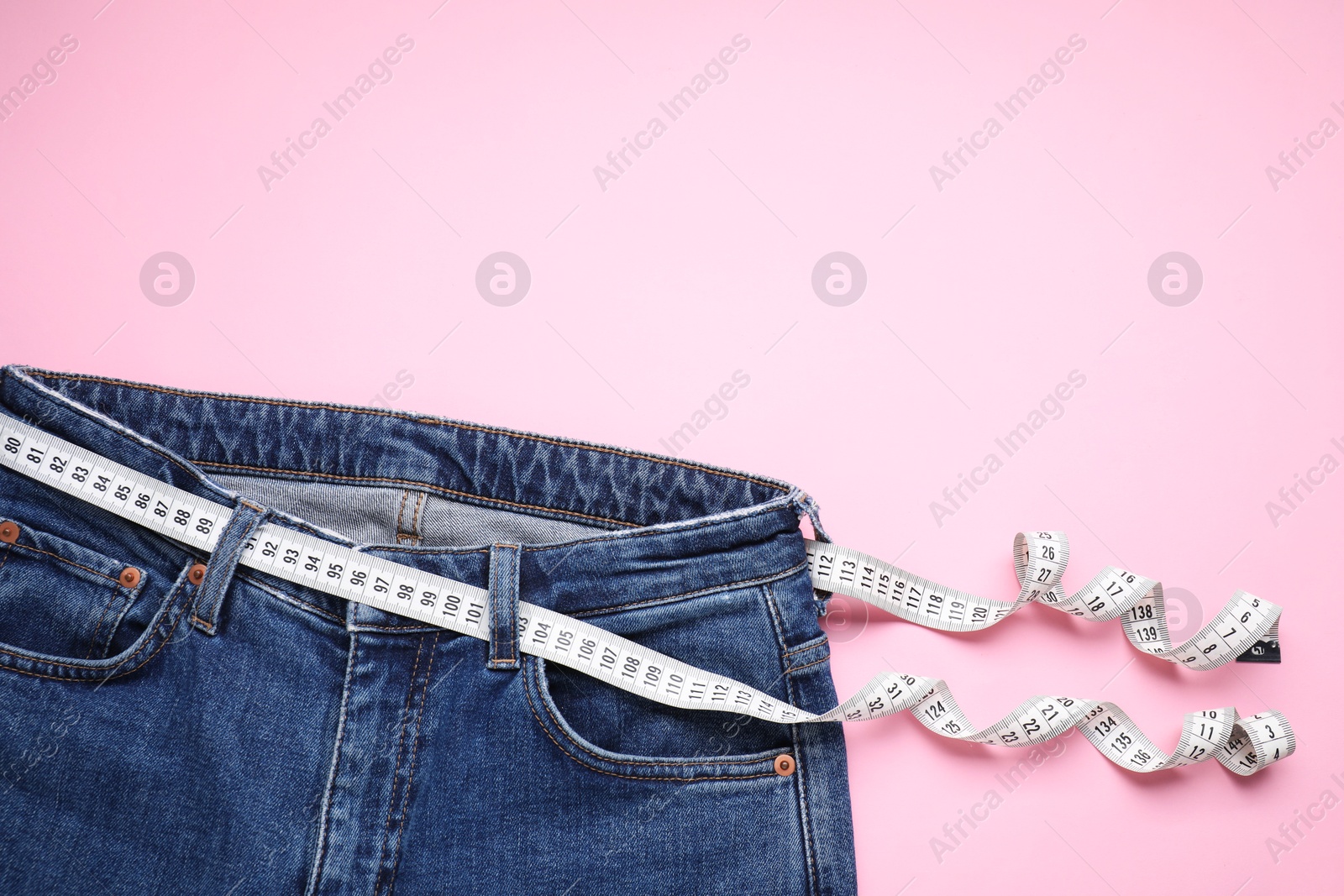 Photo of Jeans and measuring tape on pink background, top view. Space for text