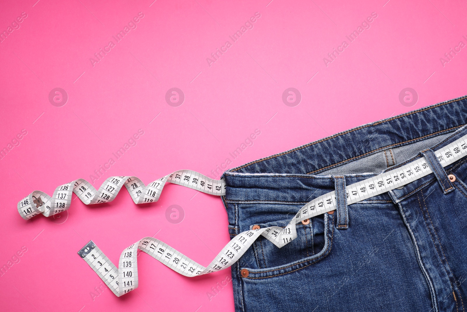 Photo of Jeans and measuring tape on pink background, top view. Space for text