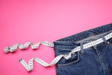 Photo of Jeans and measuring tape on pink background, top view. Space for text