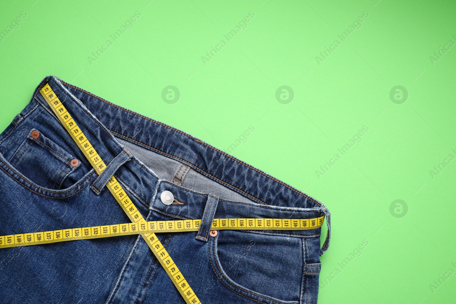 Photo of Jeans and measuring tape on light green background, top view. Space for text