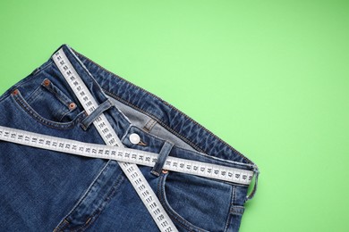 Photo of Jeans and measuring tape on light green background, top view. Space for text