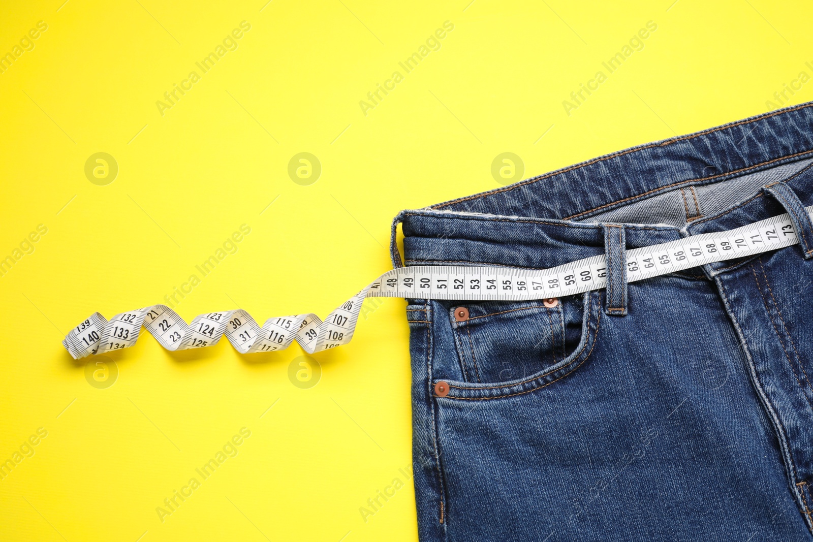 Photo of Jeans and measuring tape on yellow background, top view. Space for text