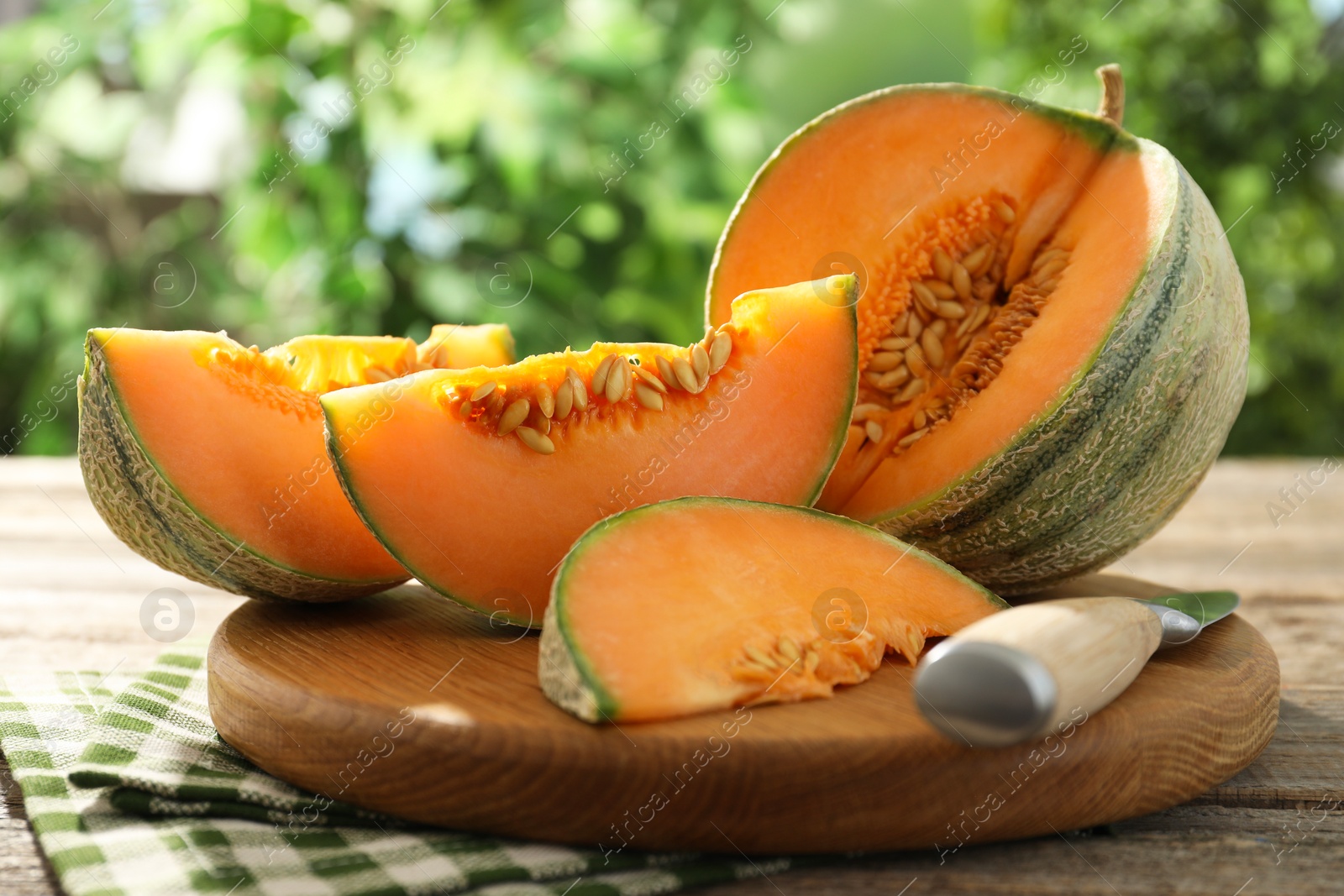 Photo of Cut ripe Cantaloupe melon and knife on wooden table outdoors, closeup