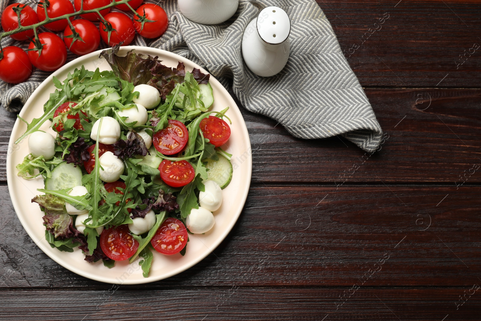 Photo of Tasty salad with arugula, lettuce, mozzarella cheese and vegetables on wooden table, flat lay. Space for text