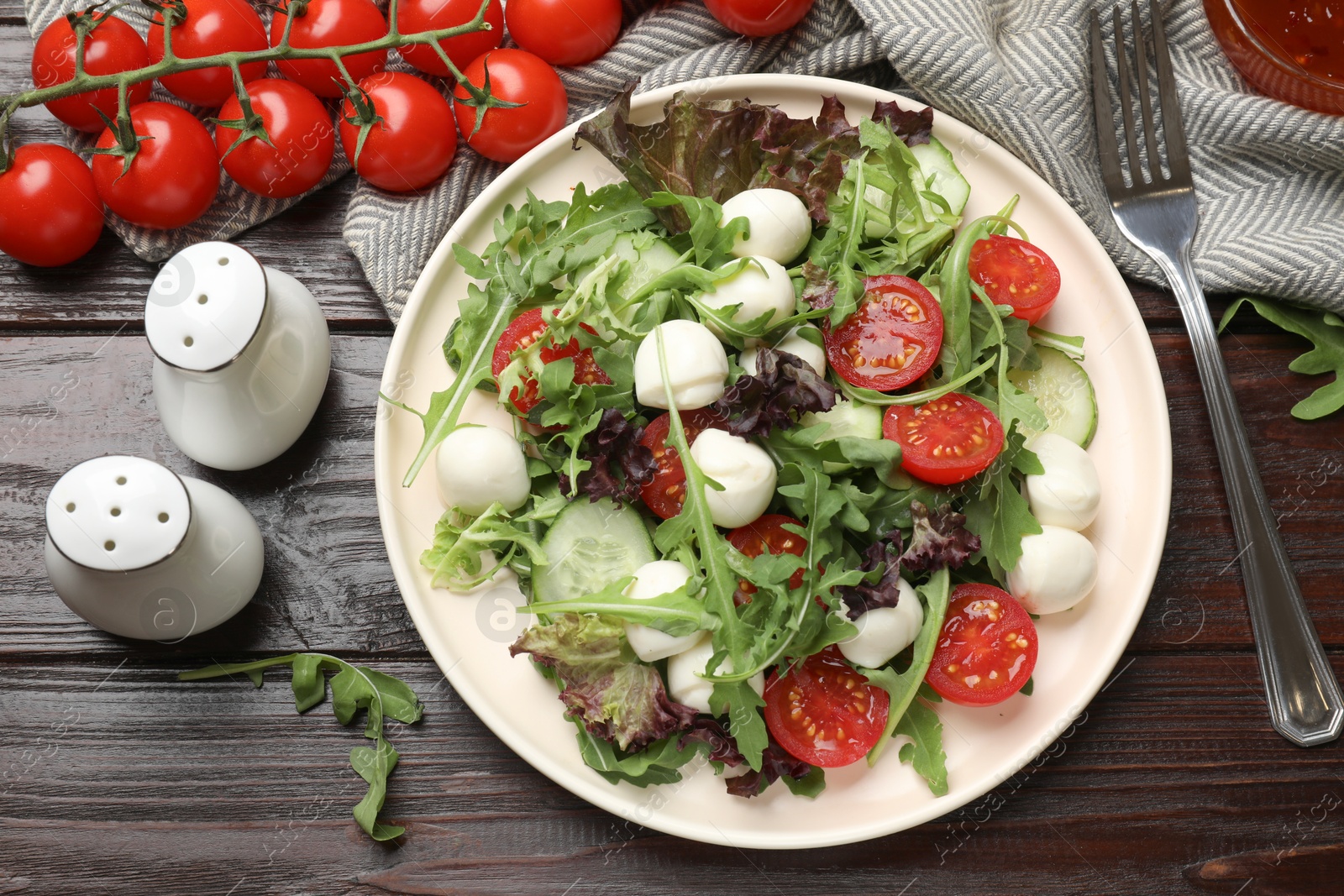 Photo of Tasty salad with arugula, lettuce, mozzarella cheese, vegetables and fork on wooden table, flat lay