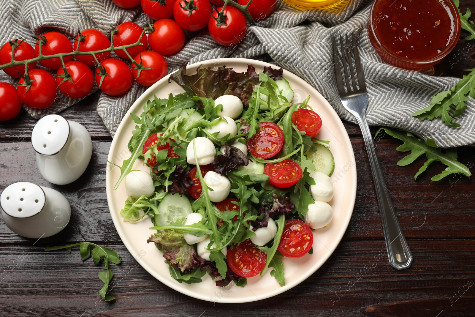 Photo of Tasty salad with arugula, lettuce, mozzarella cheese, vegetables and fork on wooden table, flat lay