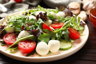 Photo of Tasty salad with arugula, lettuce, mozzarella cheese and vegetables on wooden table, closeup