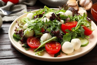 Photo of Tasty salad with arugula, lettuce, mozzarella cheese and vegetables on wooden table, closeup