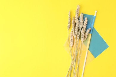 Photo of Ears of wheat and Ukrainian national flag on yellow background, flat lay. Space for text