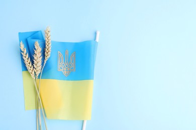 Photo of Ears of wheat and Ukrainian flag on light blue background, top view. Space for text