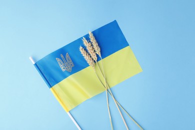 Photo of Ears of wheat and Ukrainian flag on light blue background, top view