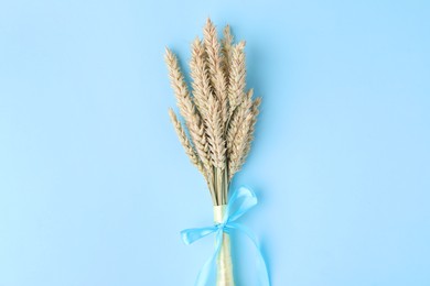 Photo of Ears of wheat with ribbons in colors of Ukrainian national flag on light blue background, top view