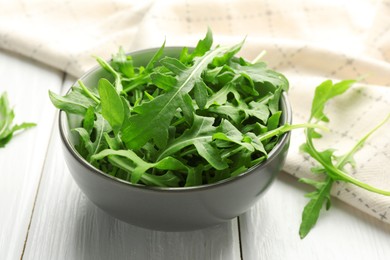 Photo of Fresh green arugula leaves in bowl on white wooden table, closeup