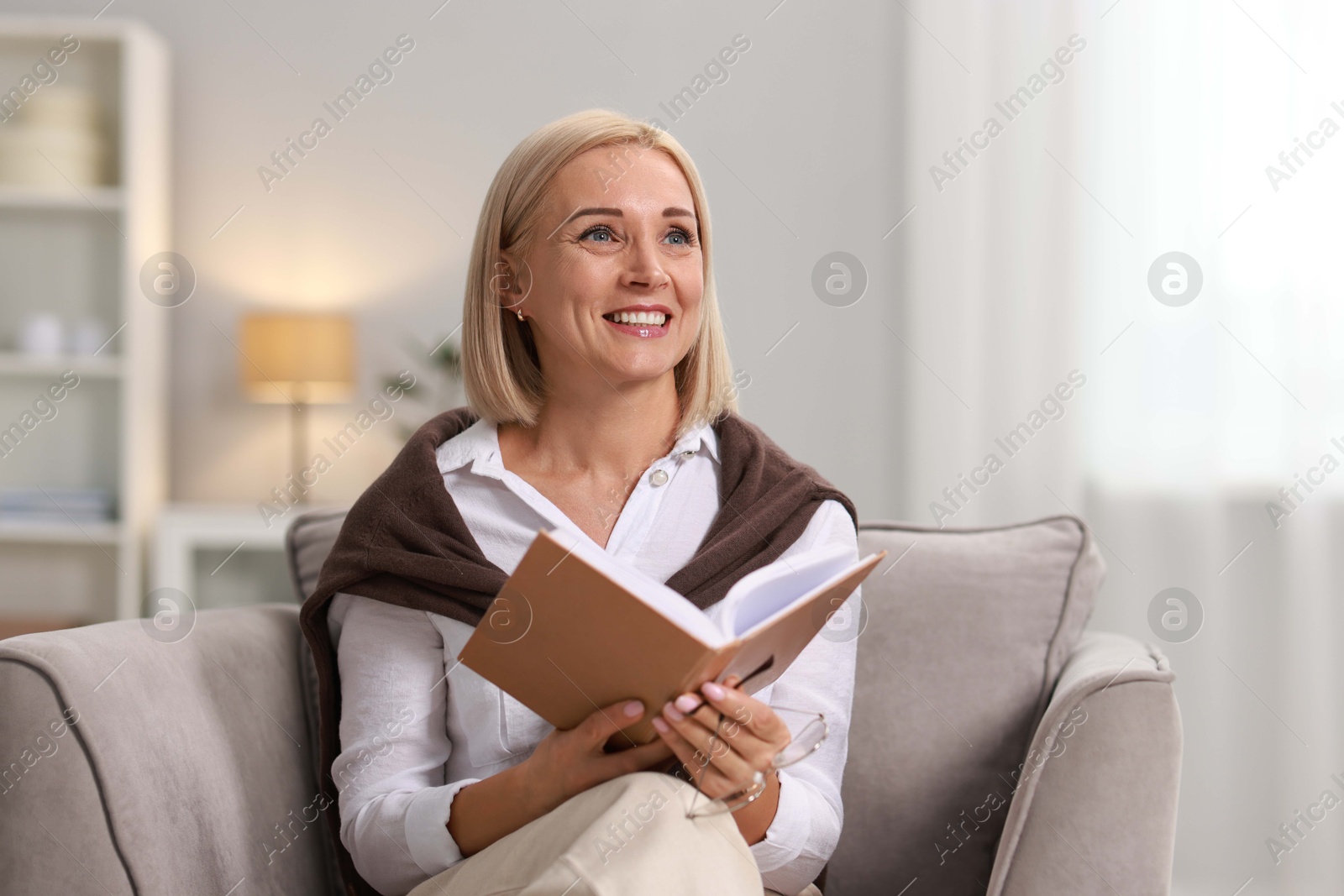 Photo of Portrait of smiling middle aged woman reading book at home