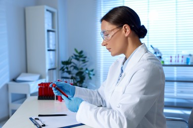 Laboratory testing. Doctor holding test tube with blood sample at table indoors