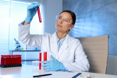 Laboratory testing. Doctor holding test tube with blood sample at table indoors