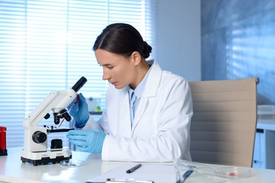 Laboratory testing. Doctor dripping blood sample onto glass slide while working with microscope at table indoors