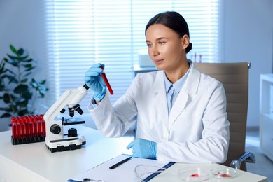 Photo of Laboratory testing. Doctor holding test tube with blood sample at table indoors