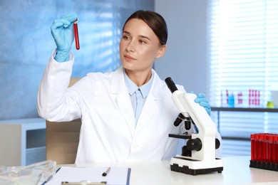 Laboratory testing. Doctor holding test tube with blood sample at table indoors