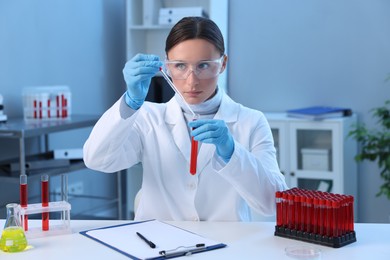 Photo of Laboratory testing. Doctor dripping blood sample into test tube at table indoors