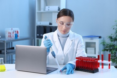 Laboratory testing. Doctor dripping blood sample into Petri dish at table indoors