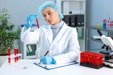 Photo of Laboratory testing. Doctor with blood sample taking notes at table indoors