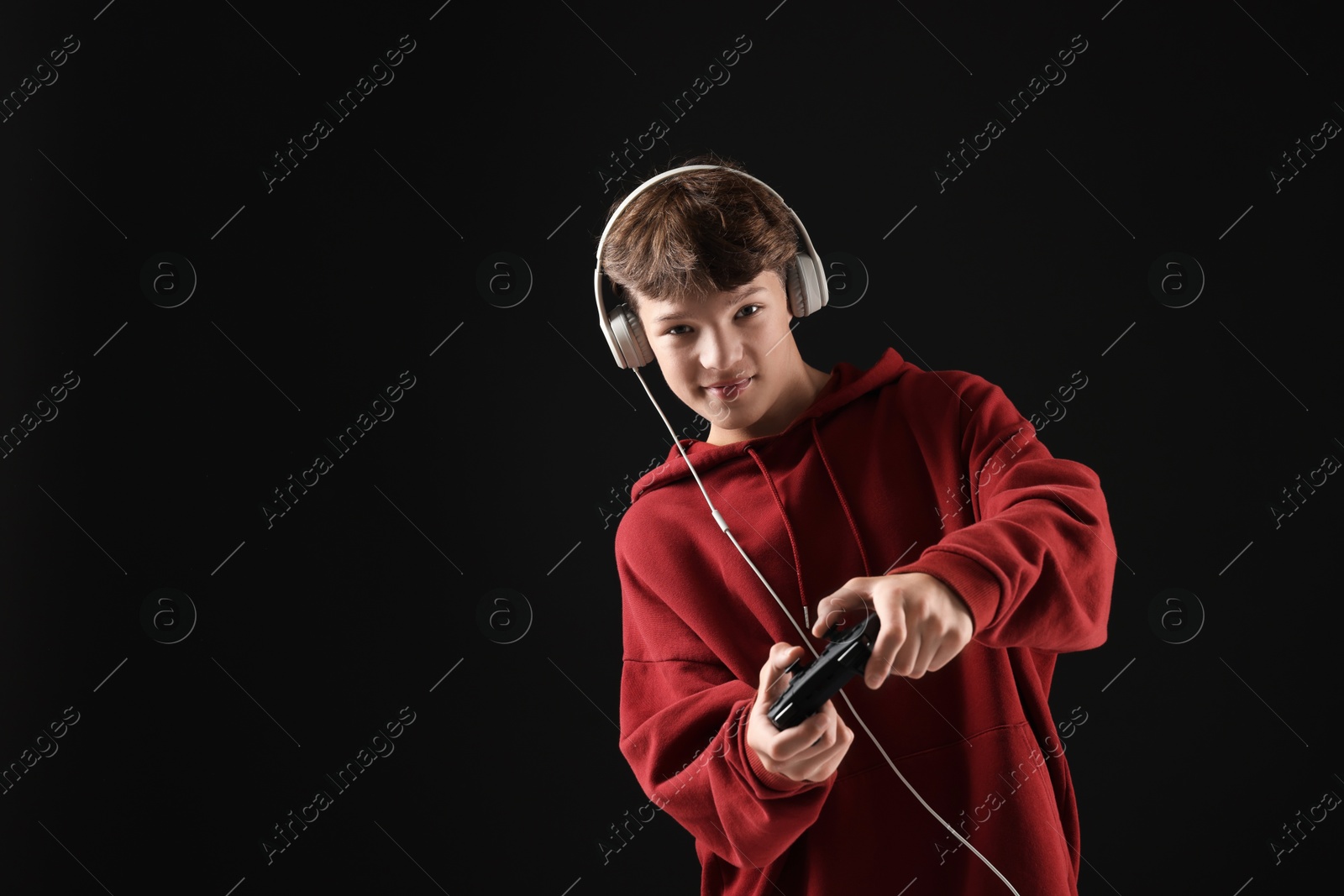 Photo of Teenage boy in headphones playing video game with controller on black background. Space for text